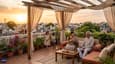 Indian multigenerational family relaxing on the large west-facing rooftop terrace of a G+2 home at sunset with pergola and potted plants