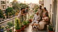 Lifestyle photo of a multi-generational Indian family gathered on the north-facing first-floor balcony — grandparents seated, parents standing, children at the railing, with the street below