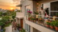 An Indian multi-generational family relaxing together on the west-facing first-floor balcony of their contemporary G+1 home at sunset, with grandparents visible on the ground floor below