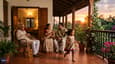 A family enjoying the west-facing verandah at dusk — single-floor home, lush landscaping, warm evening light