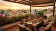 Evening lifestyle image of an Indian family on a covered west-facing rooftop terrace at golden hour, 40x50 G+3 building, comfortable outdoor furniture, warm sunset sky over a residential neighbourhood