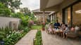 A family relaxing in the cool, shaded north-facing front garden of a 40x60 bungalow with low-maintenance plantings, stone paving, and a wide sit-out verandah