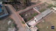 The image shows the beach house site from a bird's eye view. The site is located on a sandy beach, and it is surrounded by palm trees. The beach house is a rectangular structure, and it is located in the center of the site.